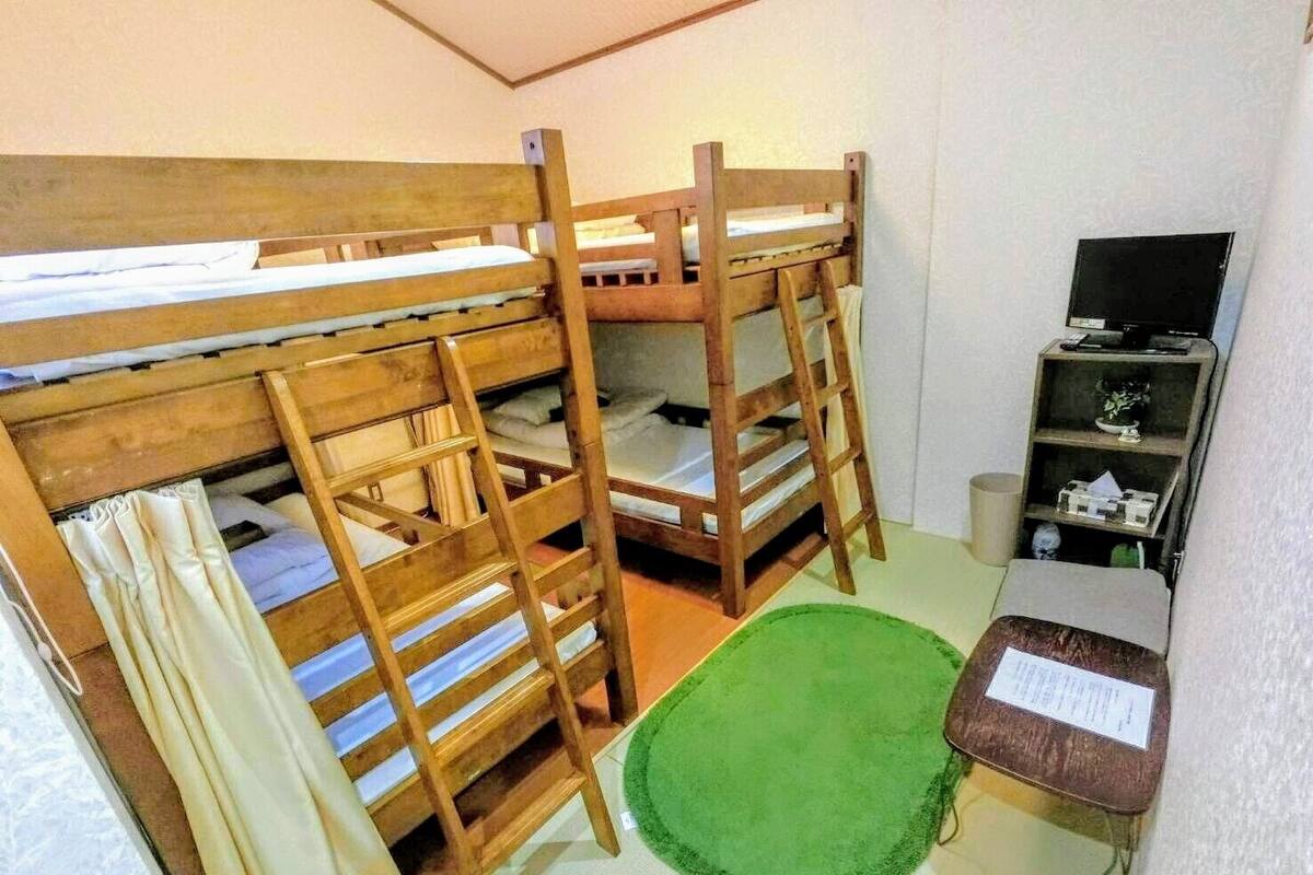 A bunk bed room with a green rug, a small table with a sign, and a shelf with items.