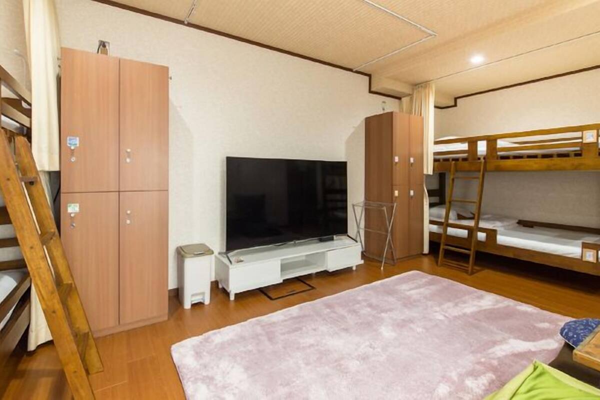 A bunk bed room with a TV, wooden wardrobe, and a small table.