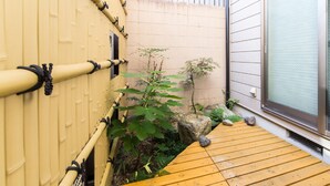 A wooden deck with a bamboo fence, a small garden with rocks and plants, and a sliding glass door. - Guesthouse Na-No-Hana - Caters to Women - Hostel (Kyoto)