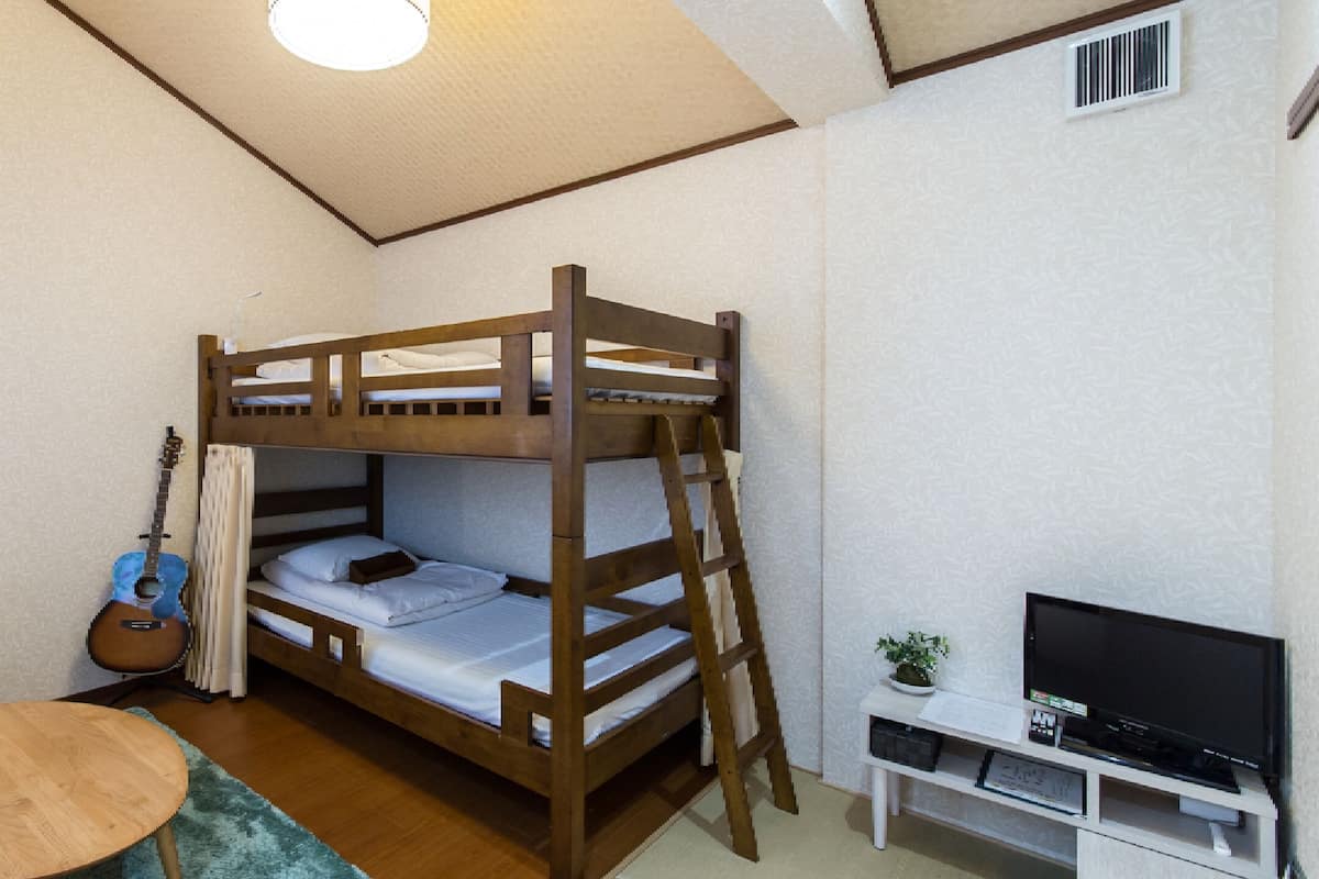 A bunk bed room with a guitar, a TV, and a small table.