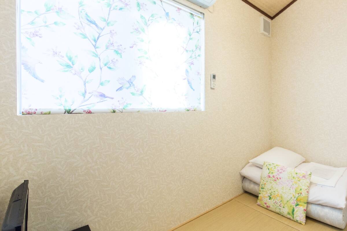 A room with a window featuring a floral pattern, a bed with white linens, and a wooden floor.