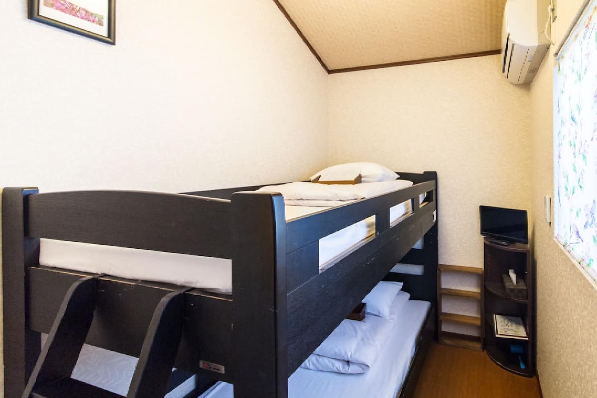 A small, single-bed room with a wooden bunk bed, a desk, and a window with floral wallpaper.