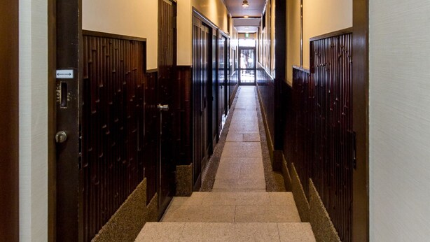 A long, narrow hallway with wooden doors on both sides, leading to a bright exit at the end. - Guesthouse Na-No-Hana - Caters to Women - Hostel (Kyoto)