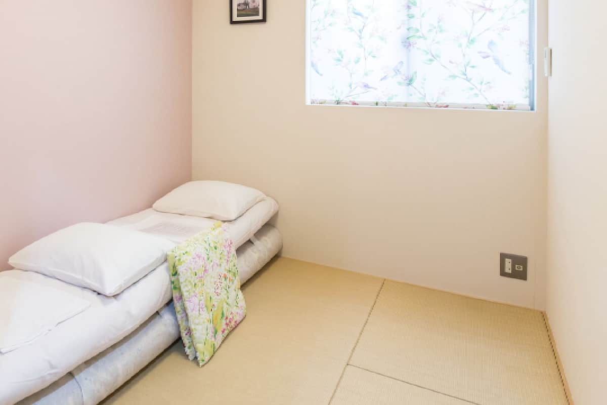 A small, single-bed room with a window, a power outlet, and a picture on the wall.