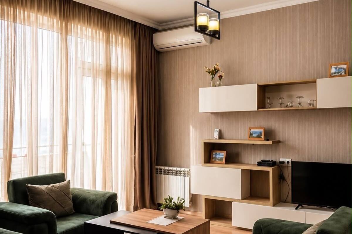 En moderne stue med grønne sofaer, et træbord, et fladskærms-tv og indbyggede reoler.