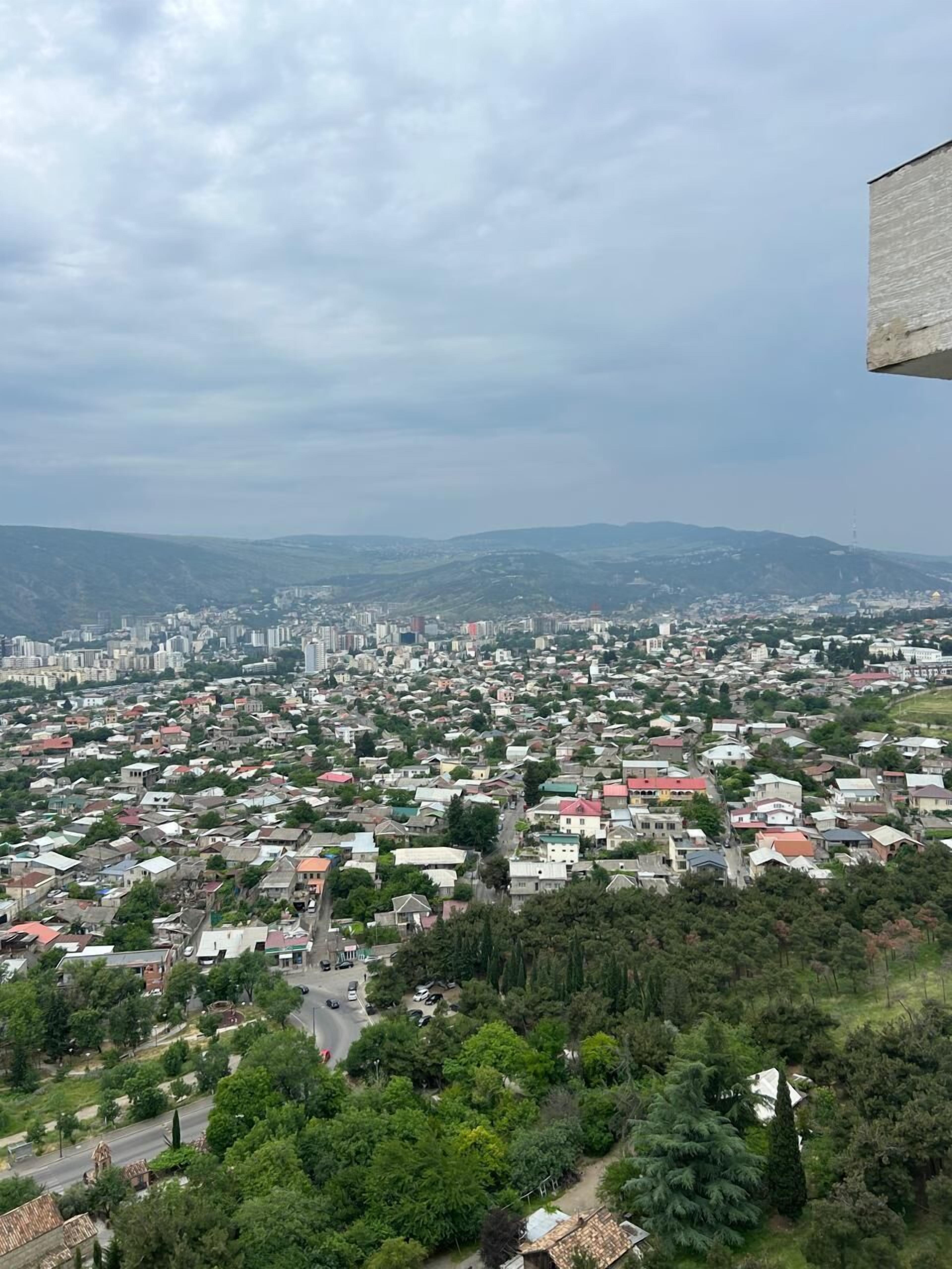 A panoramic view of a cityscape with dense residential buildings, a prominent church, and surrounding hills.