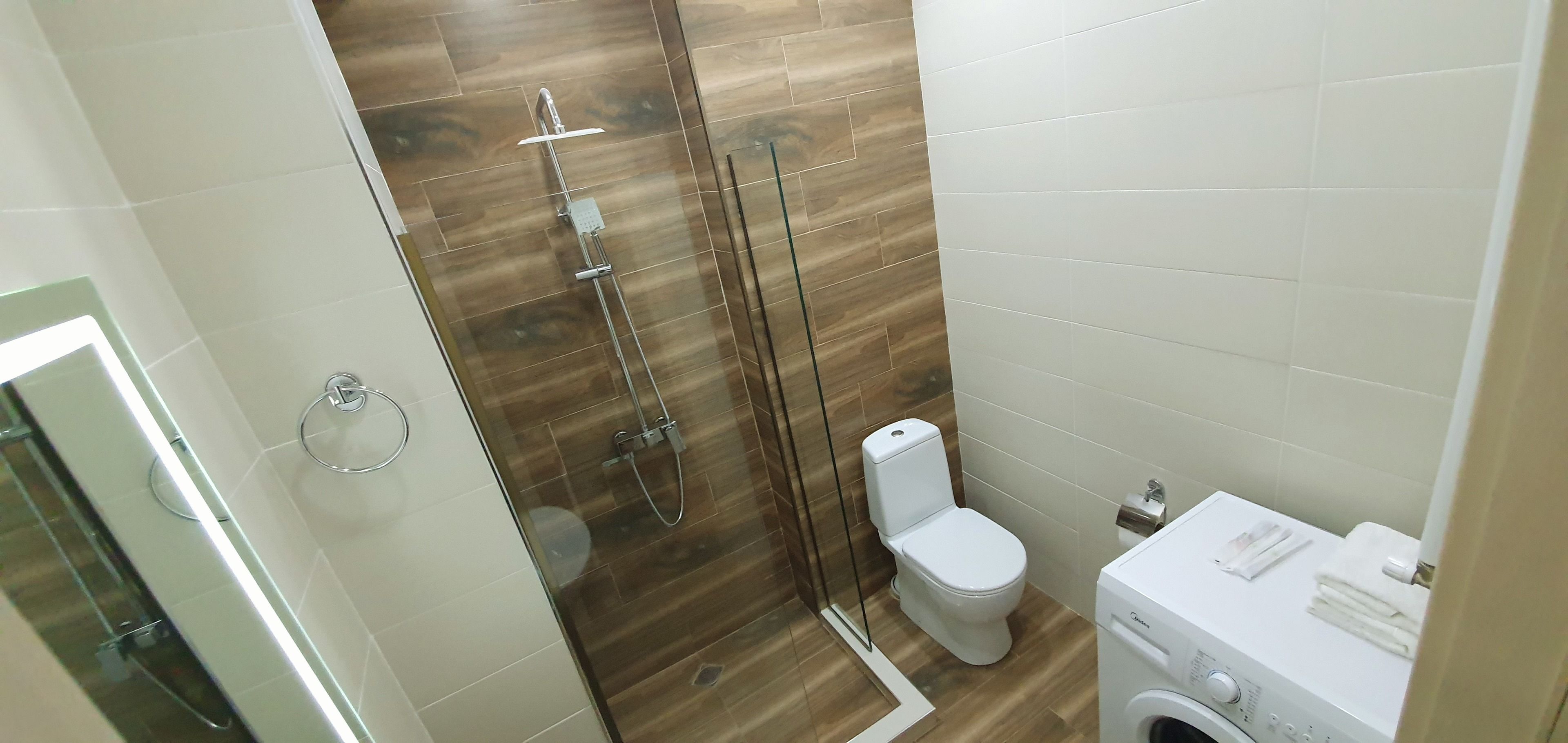A modern bathroom with a glass-enclosed shower, a toilet, and a washing machine.
