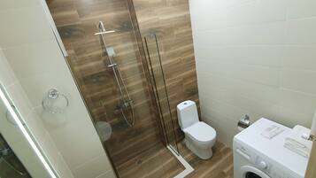 A modern bathroom with a glass-enclosed shower, a toilet, and a washing machine.