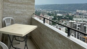 Un balcón con una mesa y dos sillas, con vistas a un paisaje urbano de edificios y colinas.