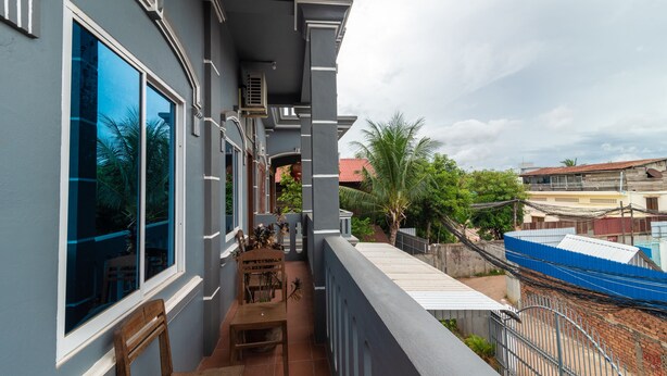 Un balcón con una silla y mesa de madera, con vistas a una zona residencial con casas y una valla azul.