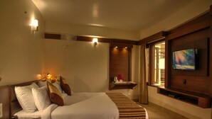 A hotel room with a large bed, a TV mounted on the wall, a bedside table with a lamp, and a window with curtains. - The Palm Hotel (Nainital)