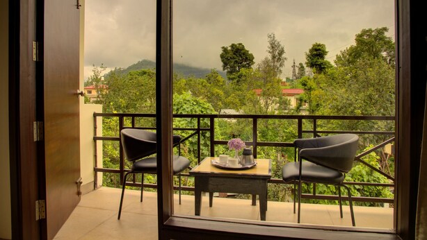 A balcony with two chairs and a small table, overlooking a lush green landscape with trees and distant hills. - The Palm Hotel (Nainital)