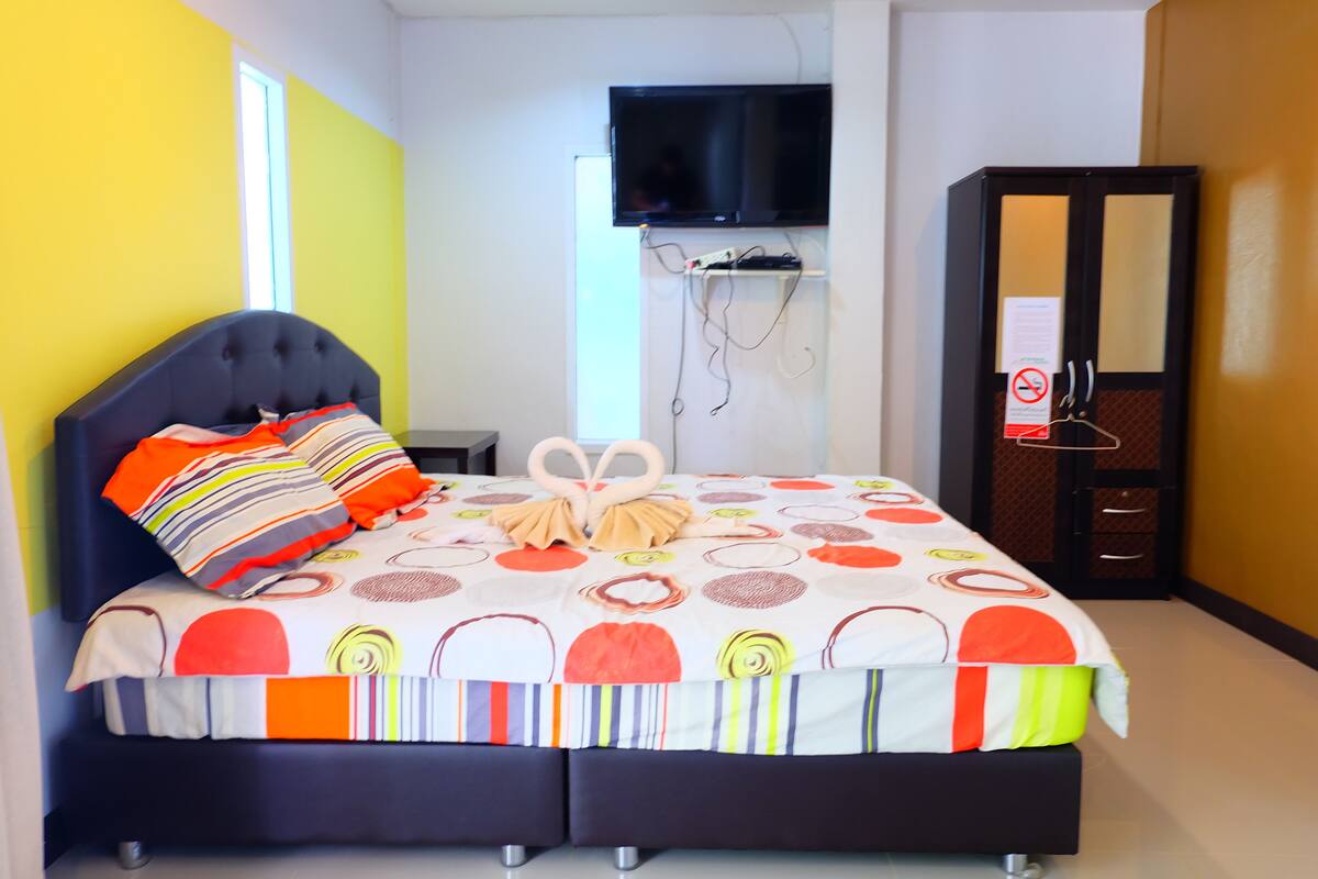 A double bed with a striped pillow, a heart-shaped pillow arrangement, and a colorful bedspread.