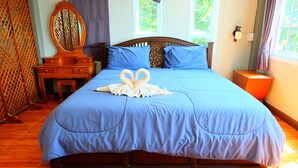 A neatly made bed with a blue bedspread, a wooden headboard, and a decorative swan-shaped towel on the bed. - Tharadol Beach Resort (Tha Sala)