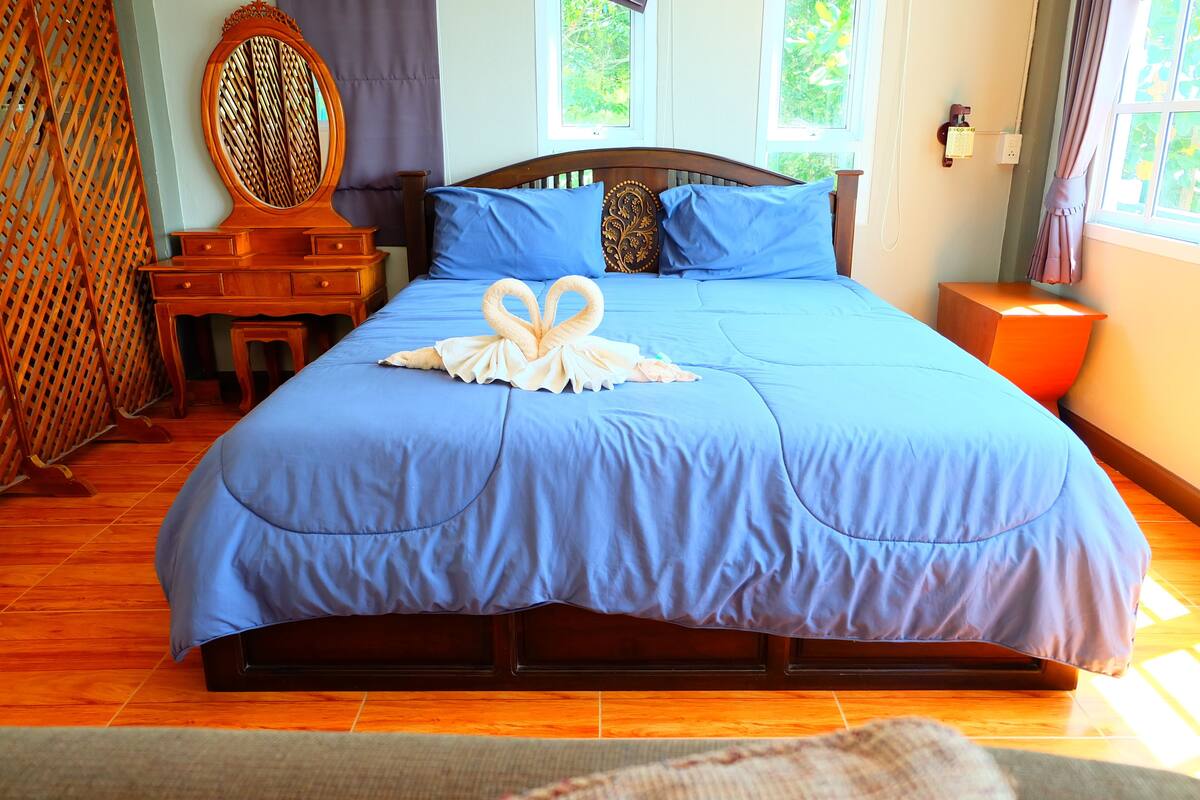 A neatly made bed with a blue bedspread, a wooden headboard, and a decorative swan-shaped towel on the bed.