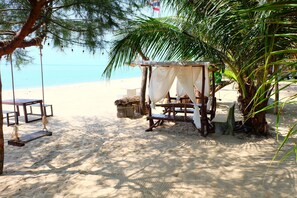 A beach setting with a wooden swing, a small covered seating area, and a bench. - Tharadol Beach Resort (Tha Sala)