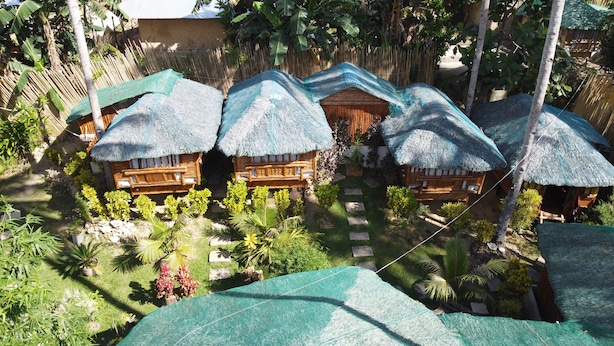 Un resort tropical con cabañas de techo de paja, muebles de madera y exuberante vegetación.