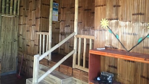 Una habitación con paredes de bambú, una escalera de madera, una estantería con un radio y un cartel en la pared.