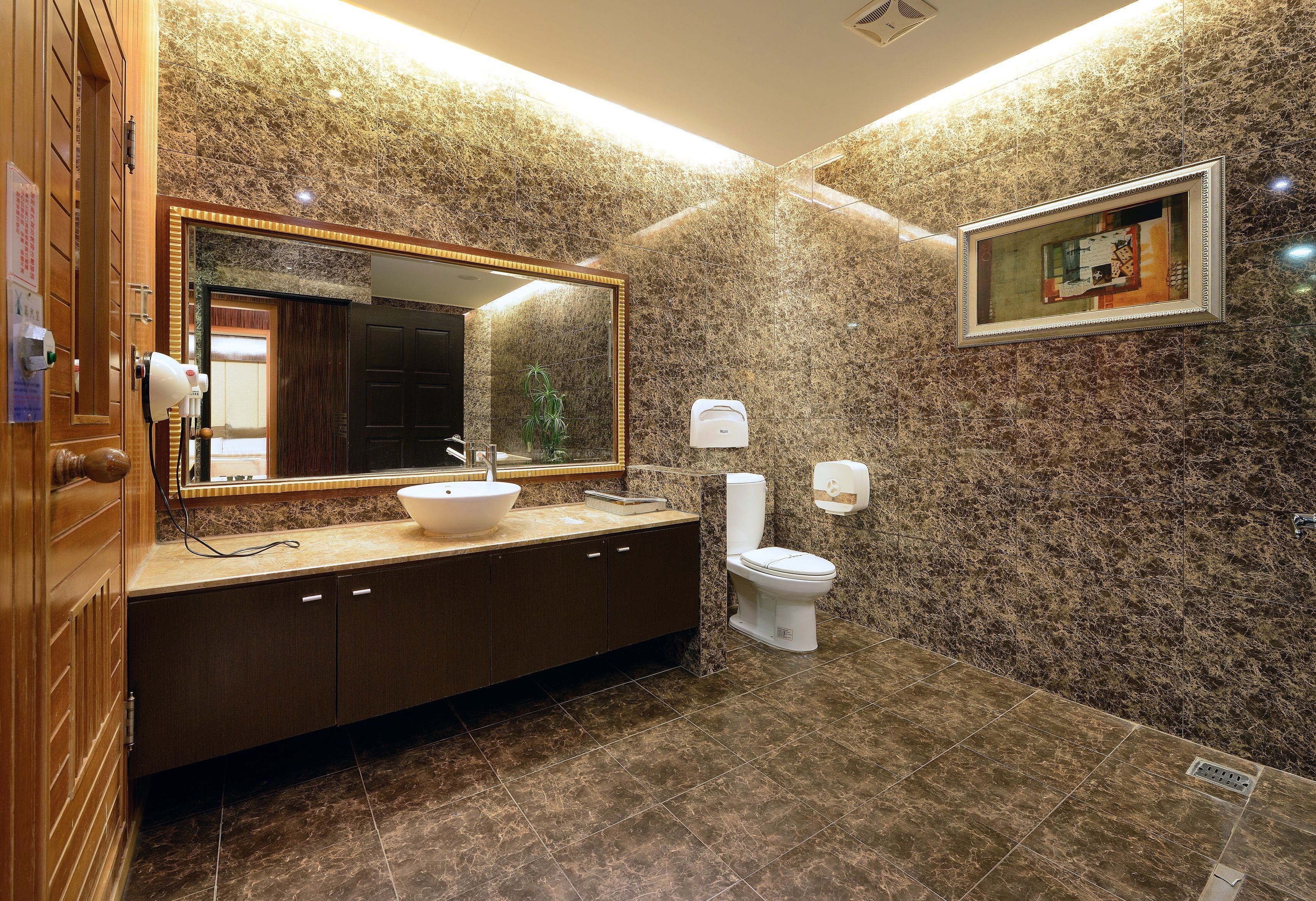 A bathroom with a marble wall, a sink, a toilet, and a mirror.