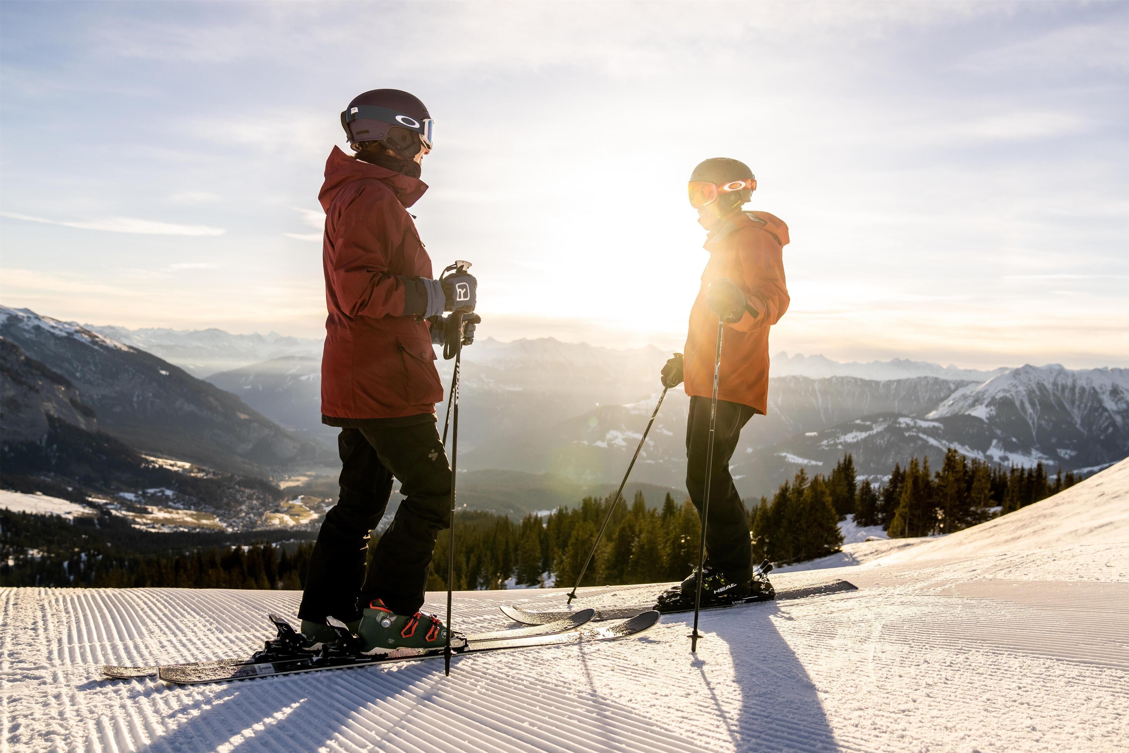 Two skiers on a snowy slope with a mountainous backdrop.