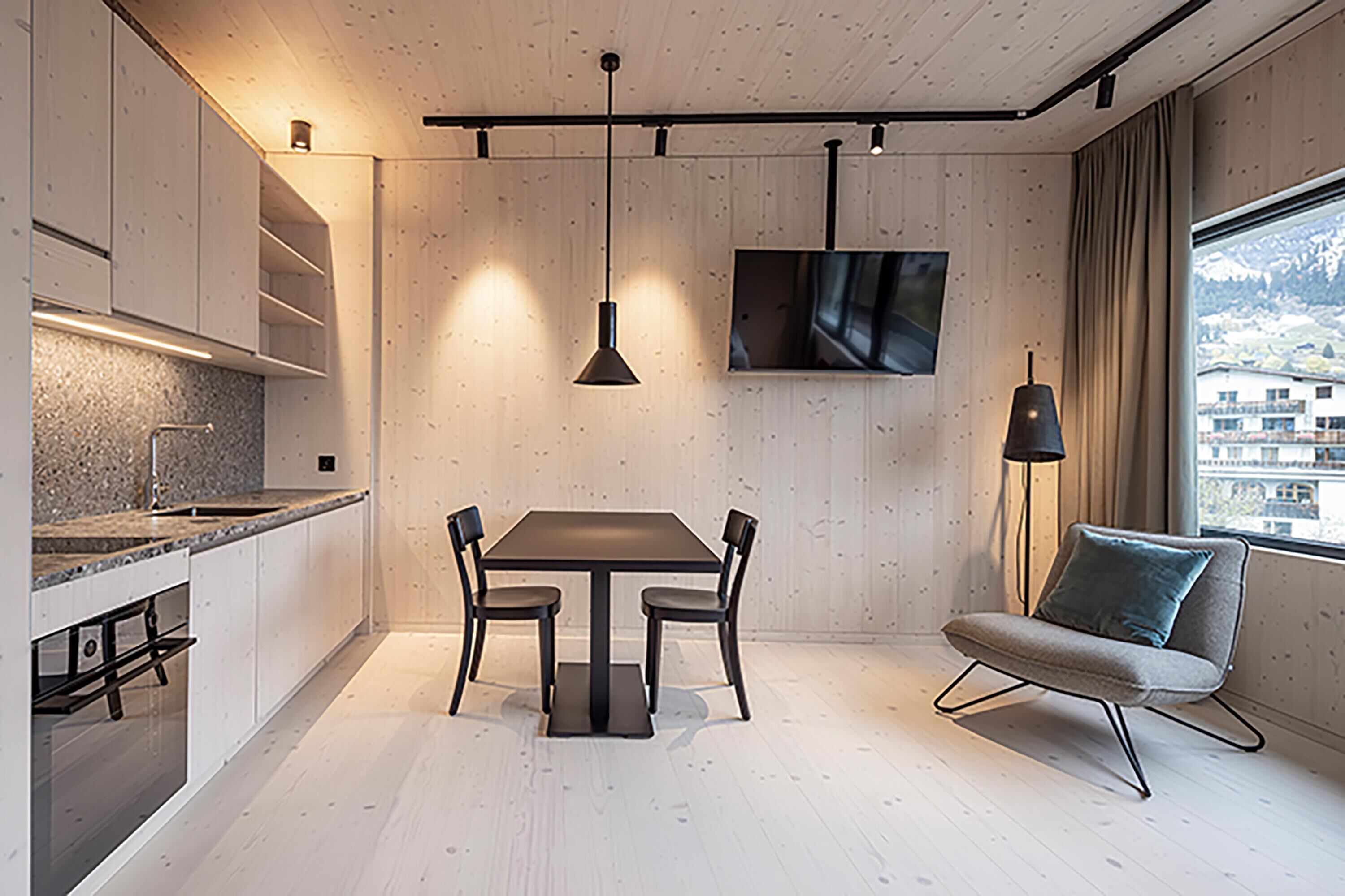 A modern kitchen with a dining area, a TV mounted on the wall, and a view of a snowy landscape through the window.