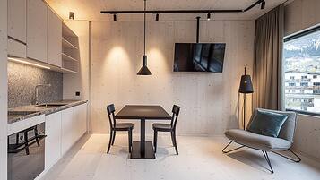 A modern kitchen with a dining area, a TV mounted on the wall, and a view of a snowy landscape through the window.