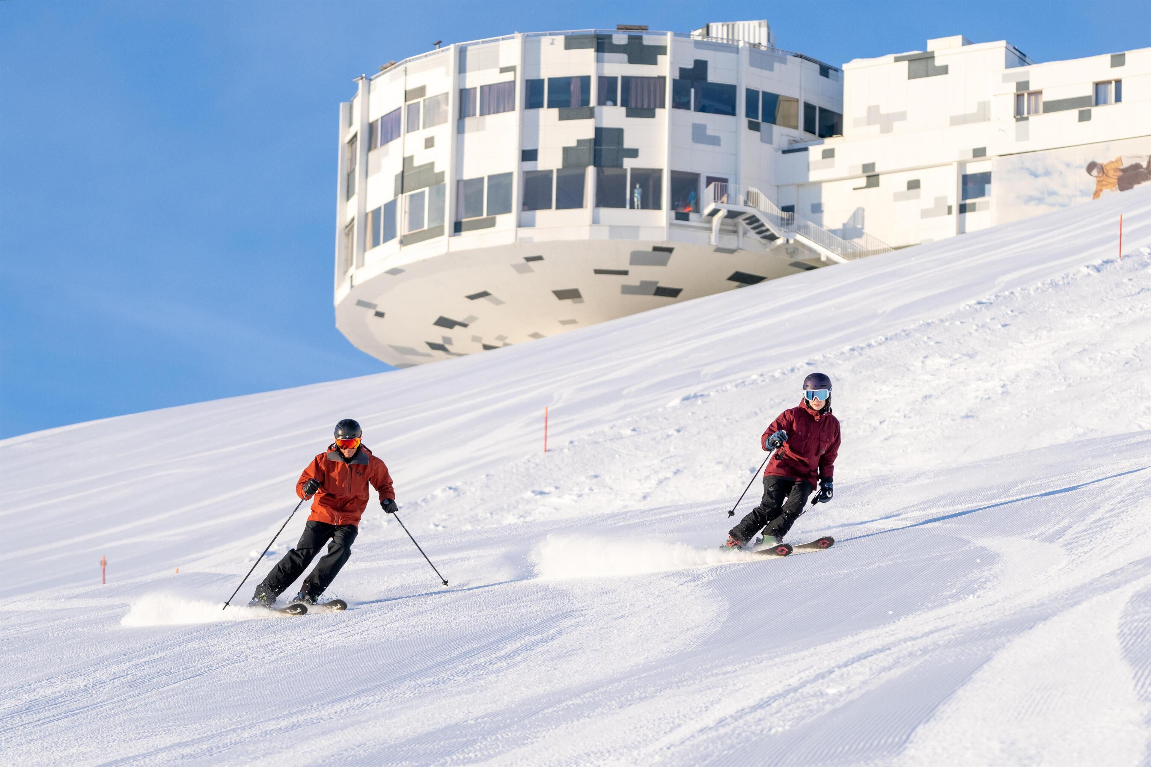 A ski slope with two skiers in red jackets.