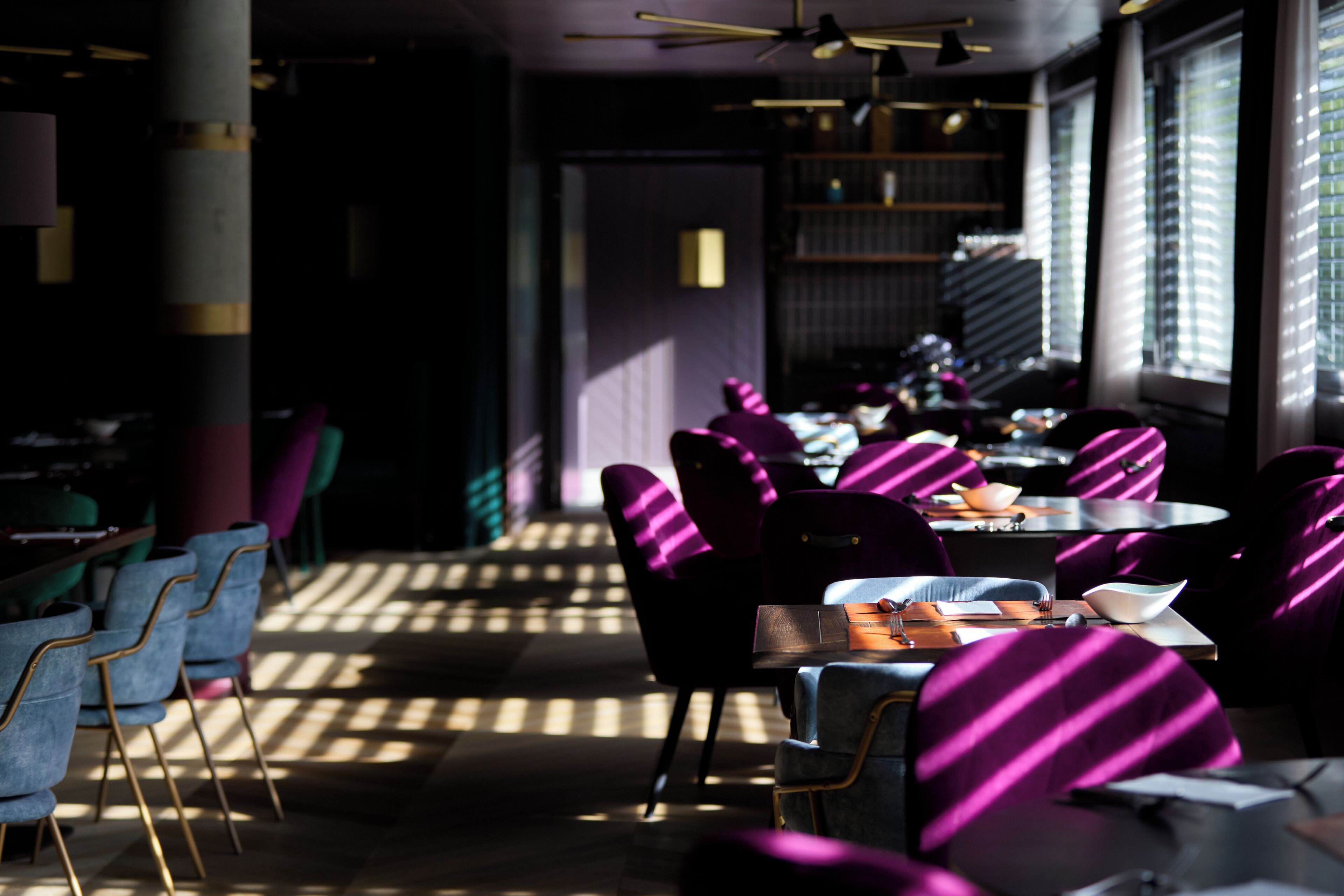 Een restaurant met paarse stoelen en tafels, een plafondventilator en grote ramen voor natuurlijk licht.