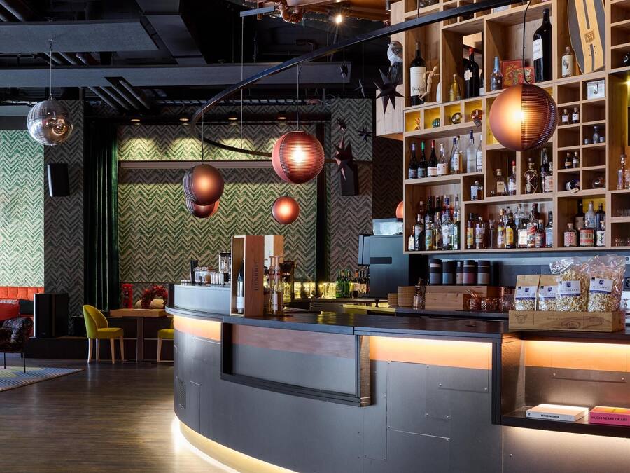 Eine Bar mit einer gebogenen Theke, Holzböden mit Flaschen und hängenden, kugelförmigen Lampen.