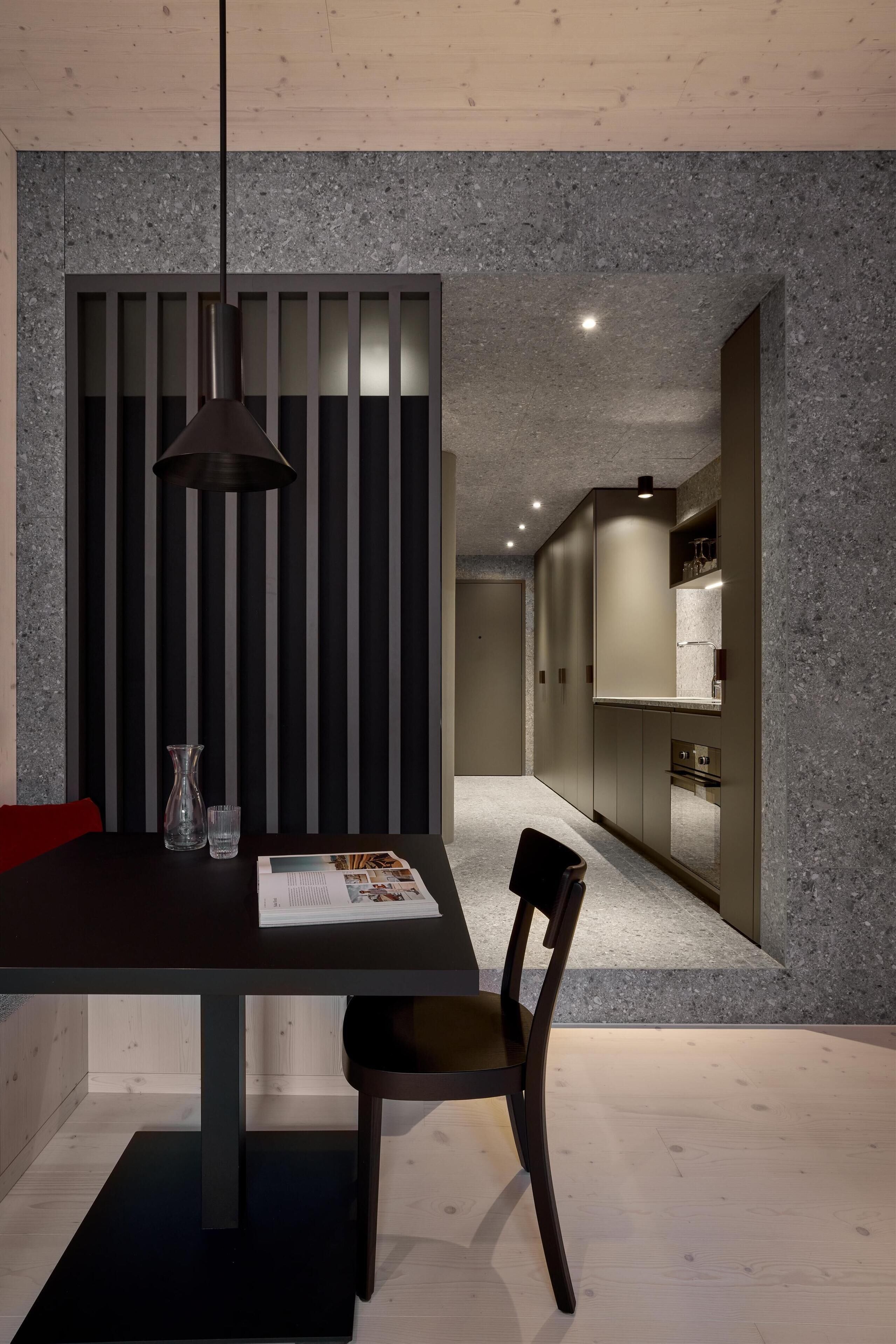 A modern dining area with a dark table, a single chair, a pendant light, and a magazine.