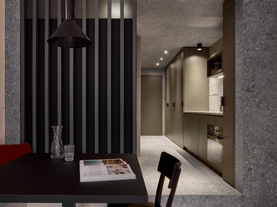 A modern dining area with a dark table, a single chair, a pendant light, and a magazine.