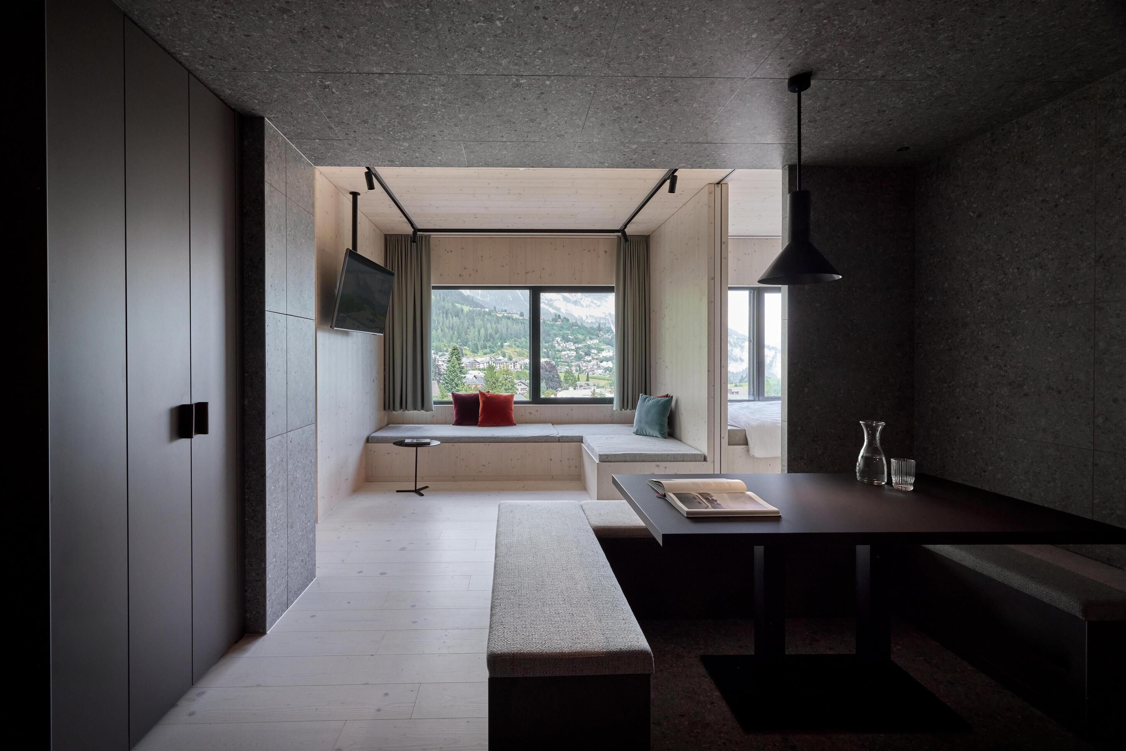Un intérieur moderne au design minimaliste, avec une grande fenêtre offrant une vue sur les montagnes, un banc intégré et un coin repas comprenant une table et des chaises.