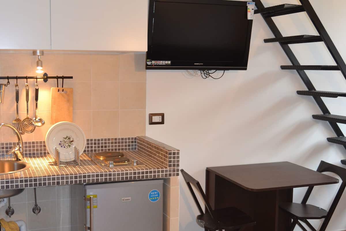 A compact kitchen with a refrigerator, sink, and a flat-screen TV mounted on the wall.