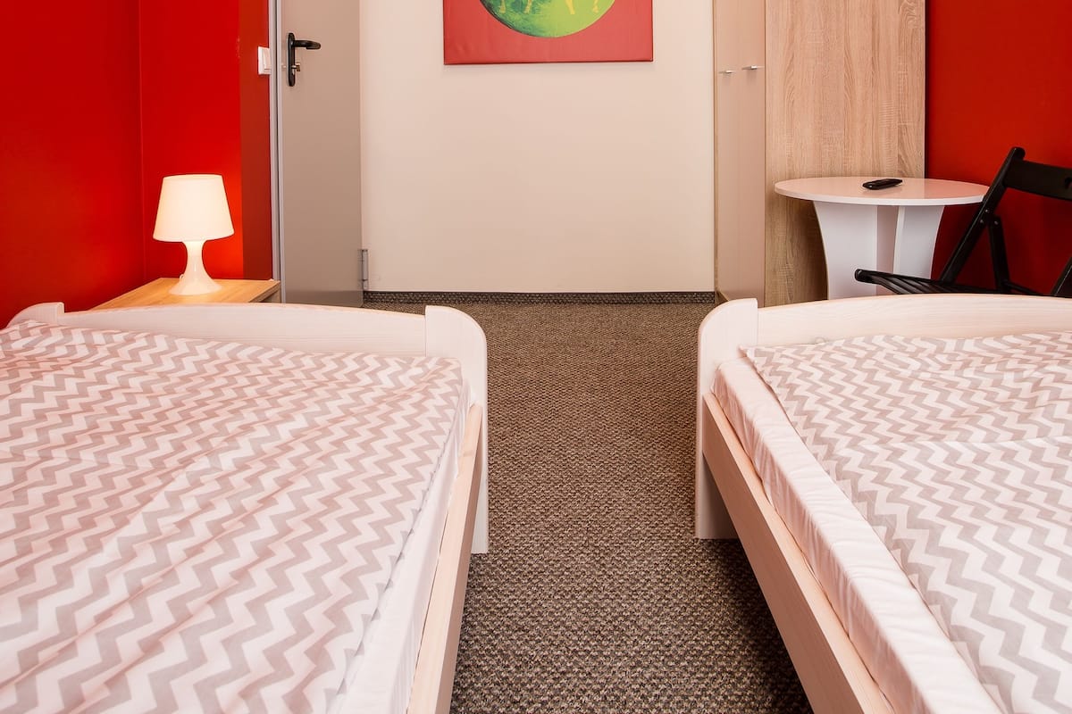 Ein Hotelzimmer mit zwei Betten, einem Schreibtisch, einem Stuhl, einer Lampe, einem Gemälde und einem Kleiderschrank.