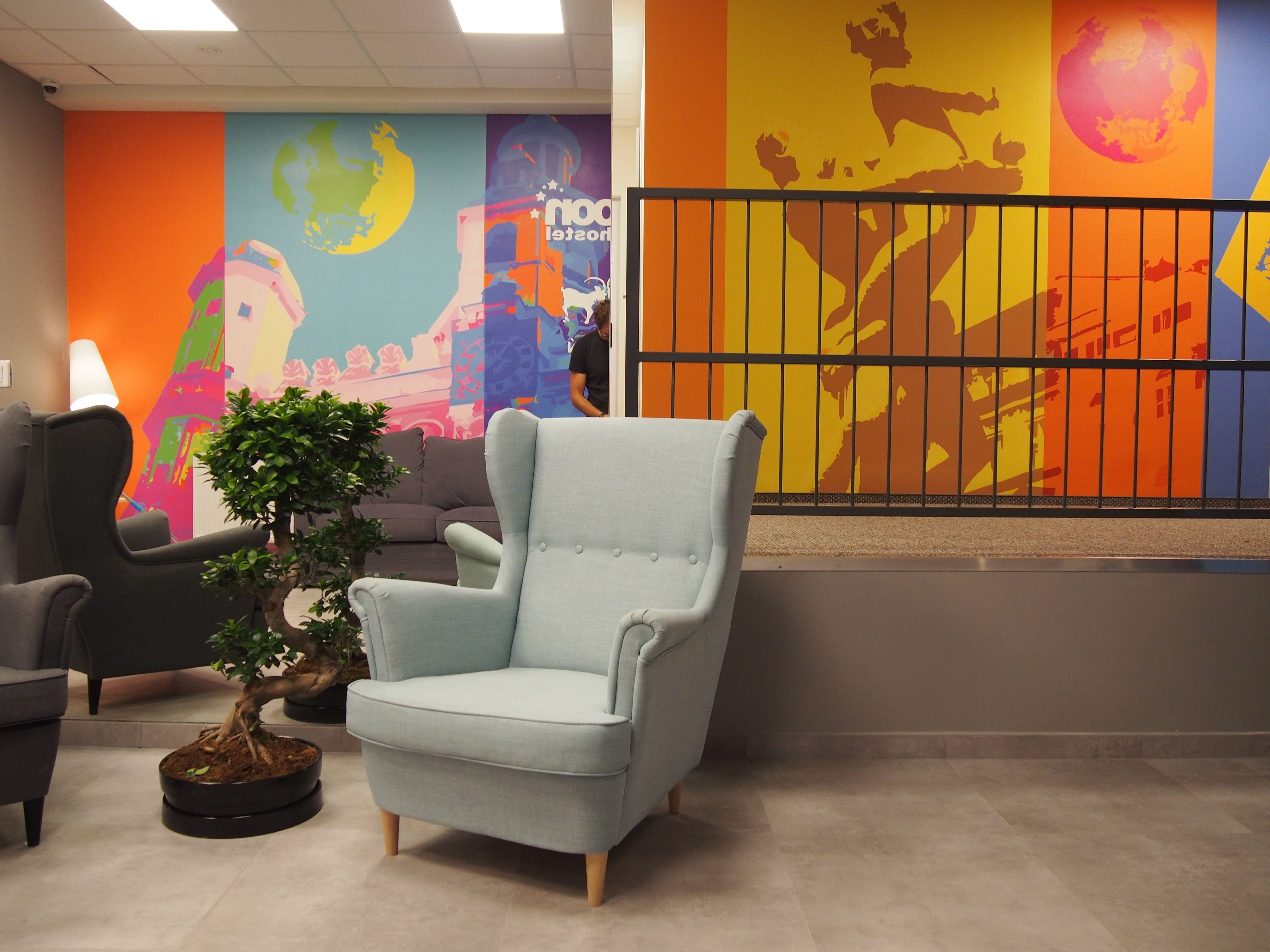 A room with a light blue armchair, a potted plant, and a colorful mural on the wall.