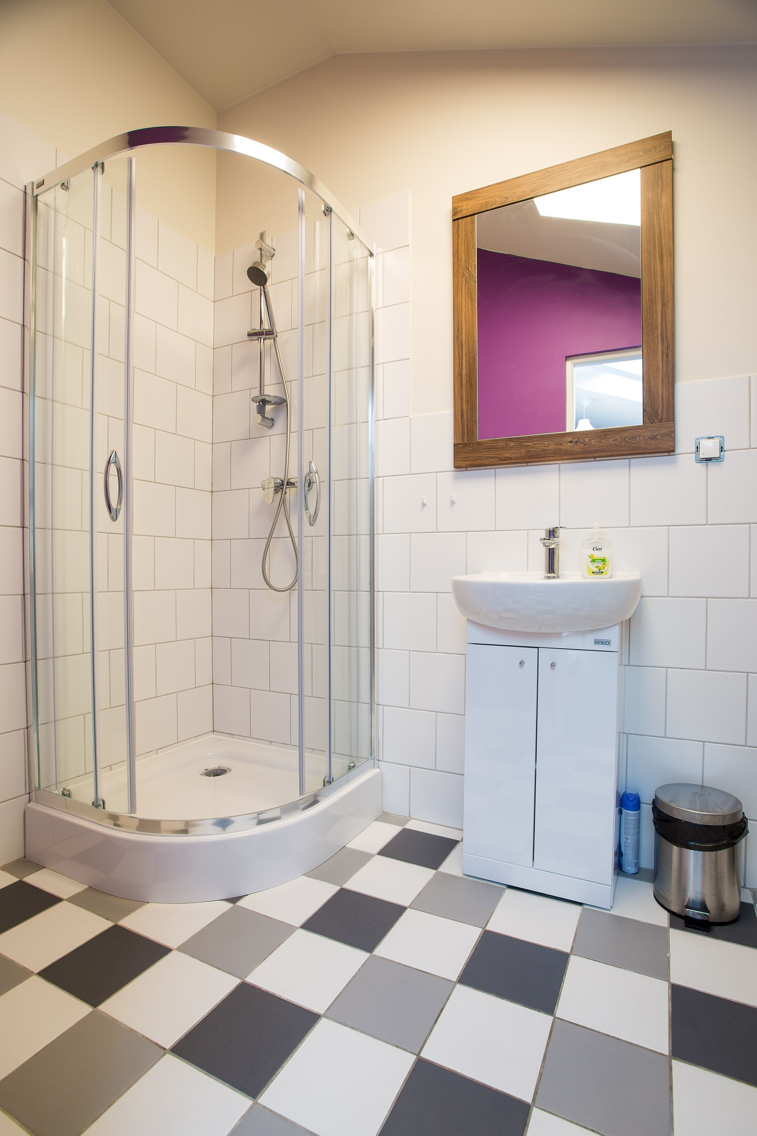 Een badkamer met een douche met glazen wand, een wastafel met spiegel erboven en een geruite vloer.