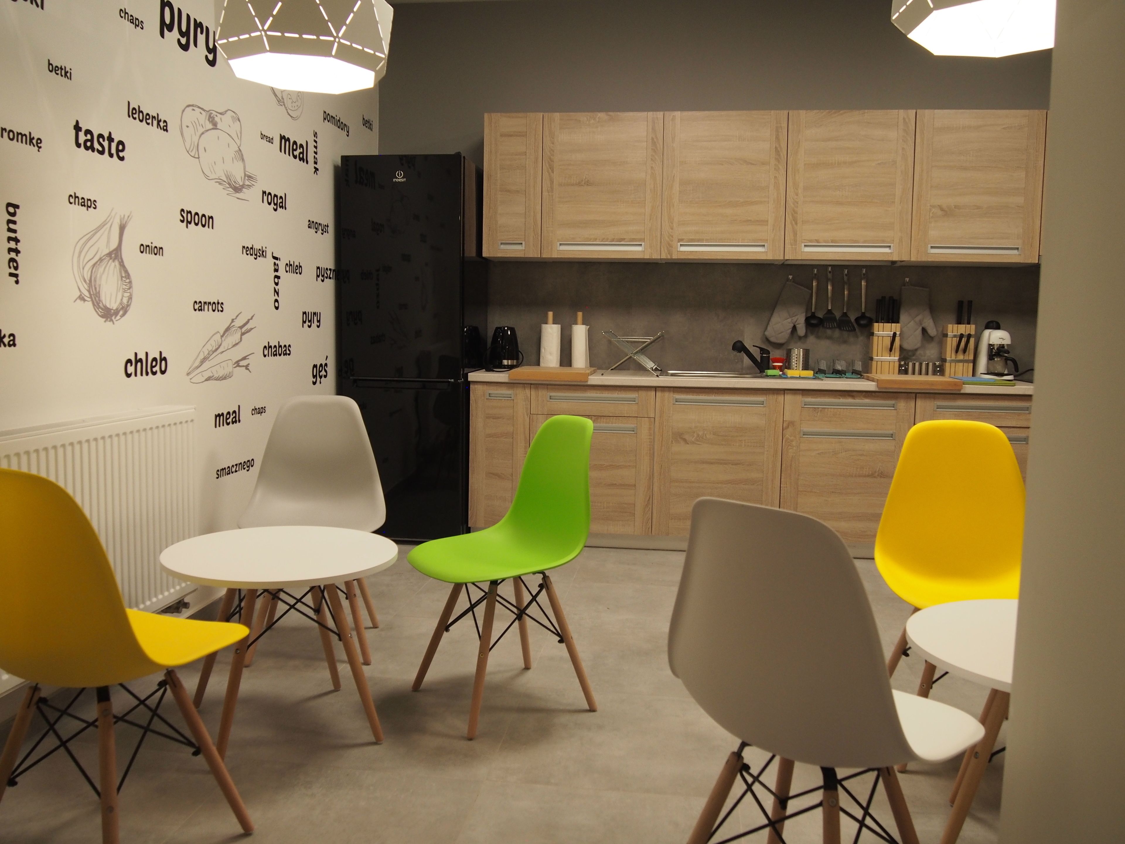 Una cocina moderna con armarios de madera, un refrigerador negro y un comedor con sillas coloridas.