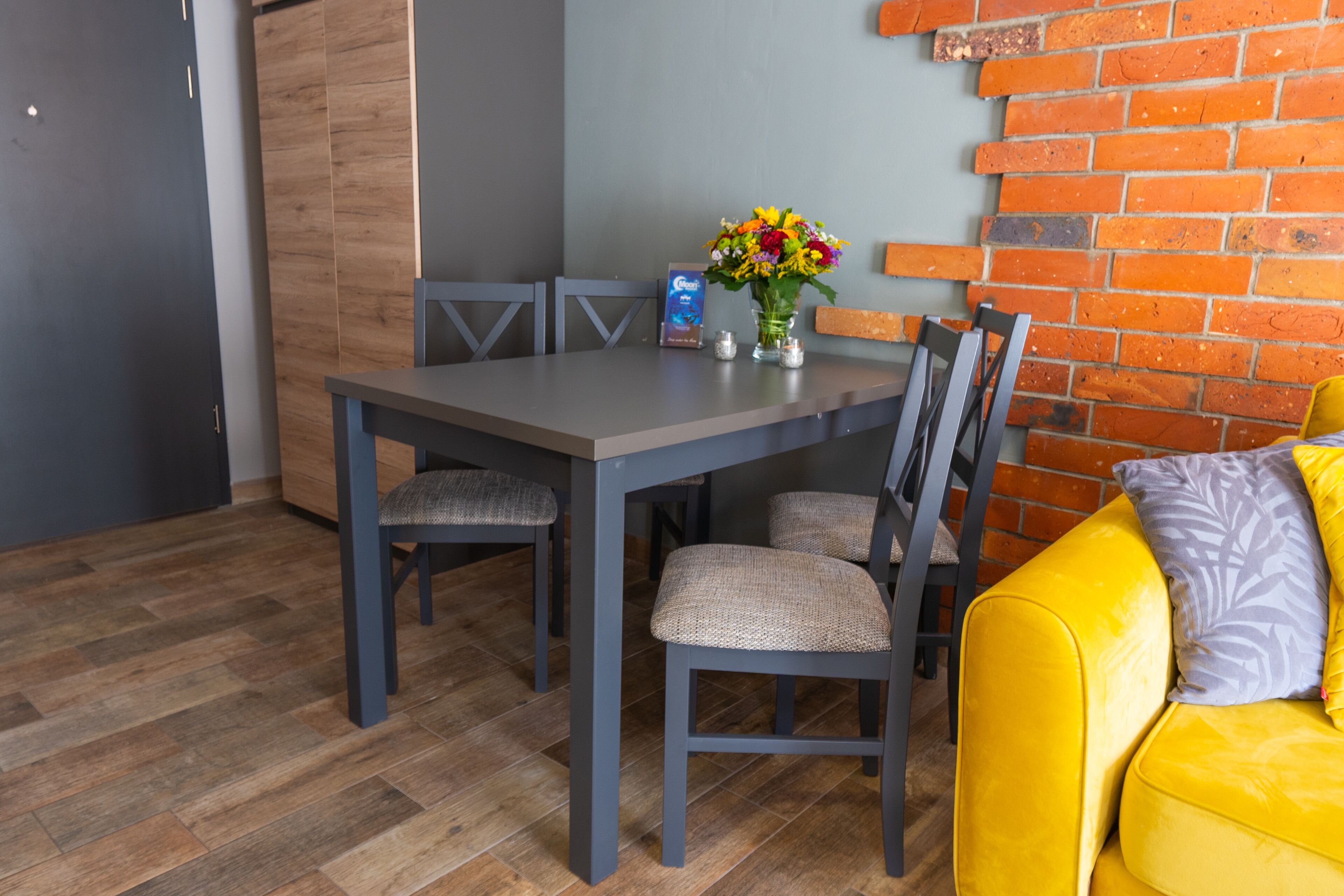 A dining area with a table and chairs, a vase with flowers, and a brick wall.