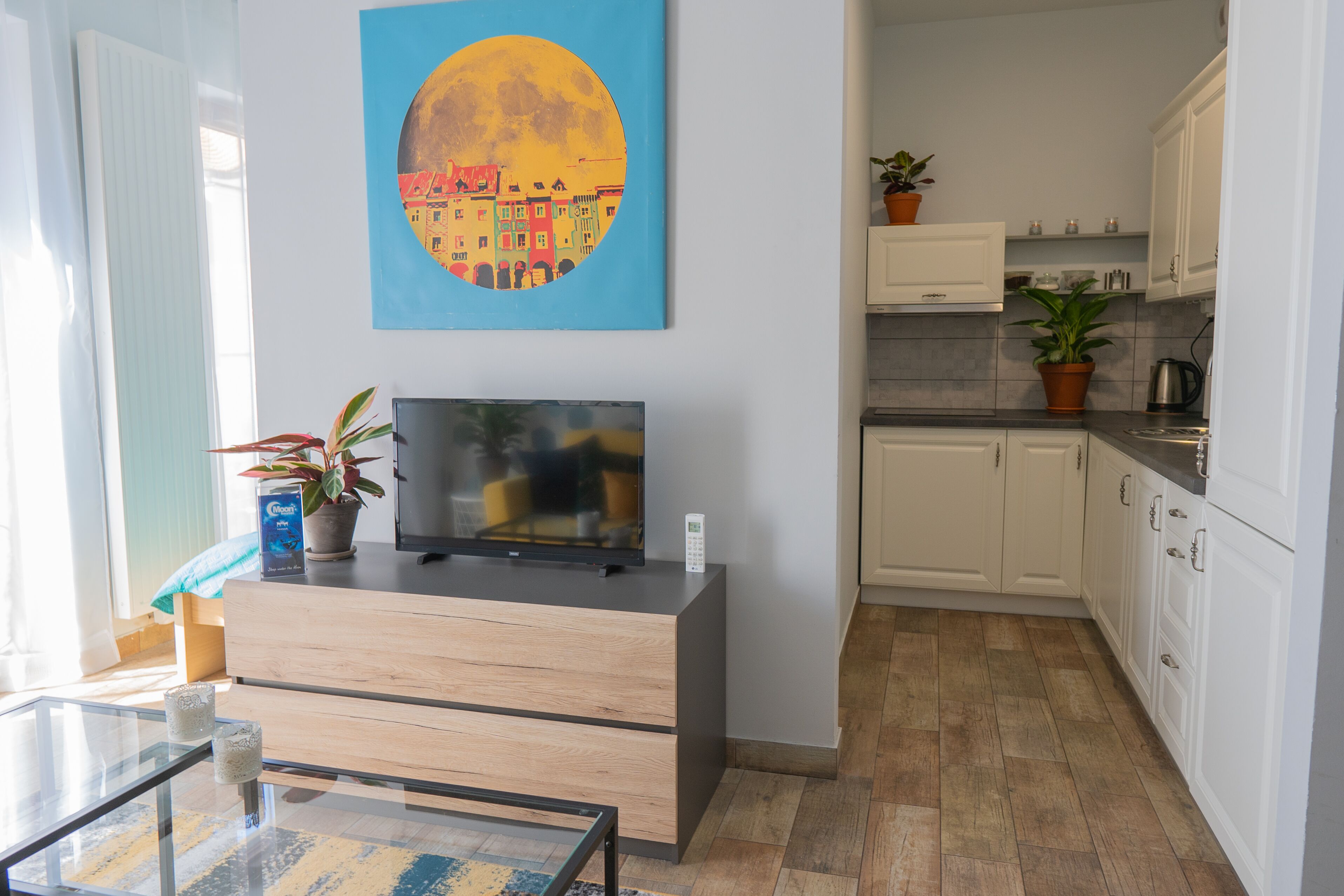 A modern living room with a flat-screen TV, a glass coffee table, and a painting on the wall.