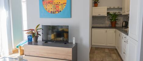 A modern living room with a flat-screen TV, a glass coffee table, and a painting on the wall.
