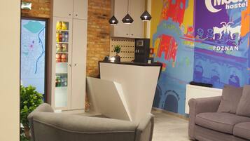 Un área de recepción con un mostrador, un sillón gris, un sofá, un mapa en la pared y un mural colorido que anuncia un albergue.