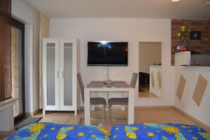A modern room with a TV mounted on the wall, a dining table with chairs, a wardrobe, and a bed with a blue and yellow patterned bedspread. - Ferienwohnung Schelsen (Moenchengladbach)