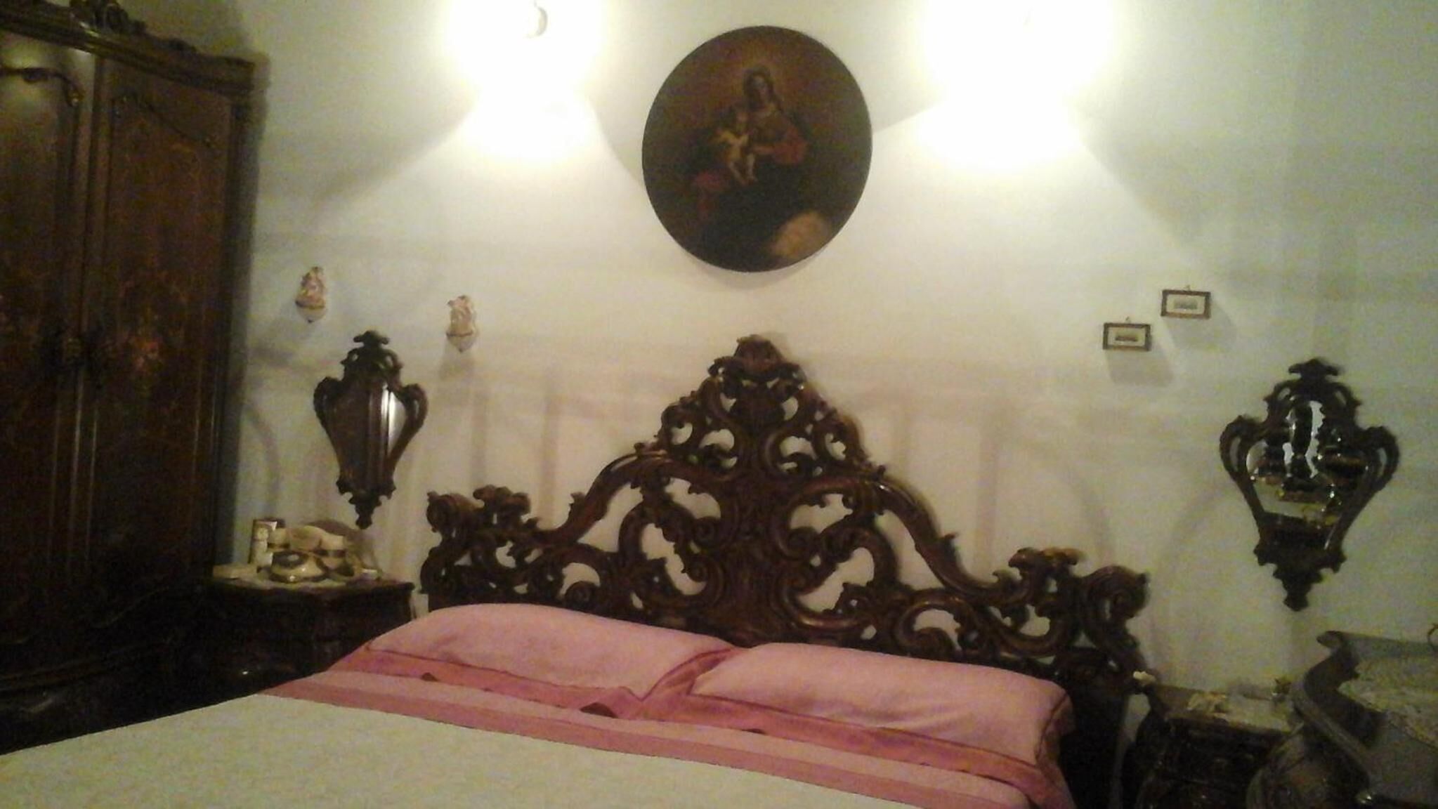 A bedroom with a large wooden bed, a wooden wardrobe, and a wall-mounted mirror.