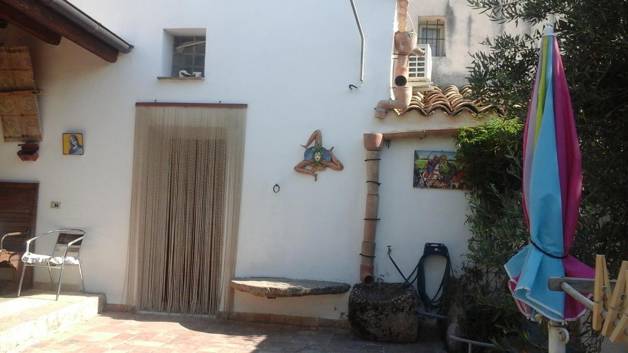 Ein Innenhof mit einer weißen Tür, einem kleinen Fenster und einem bunten Sonnenschirm.