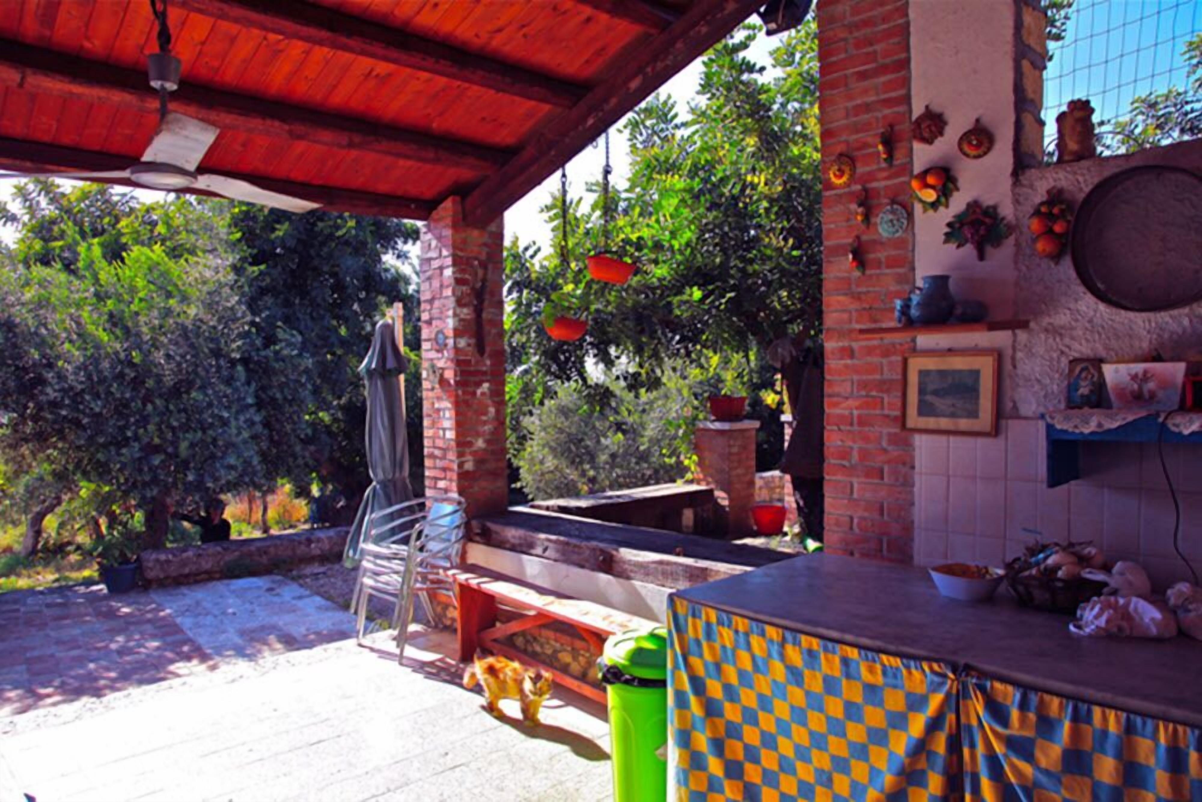 Un espace extérieur aménagé en terrasse, avec un mur en briques, un plafond en bois et une table recouverte d’une nappe à carreaux.