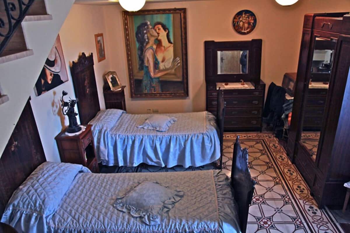 A bedroom with two beds, a dresser, a mirror, and a painting on the wall.