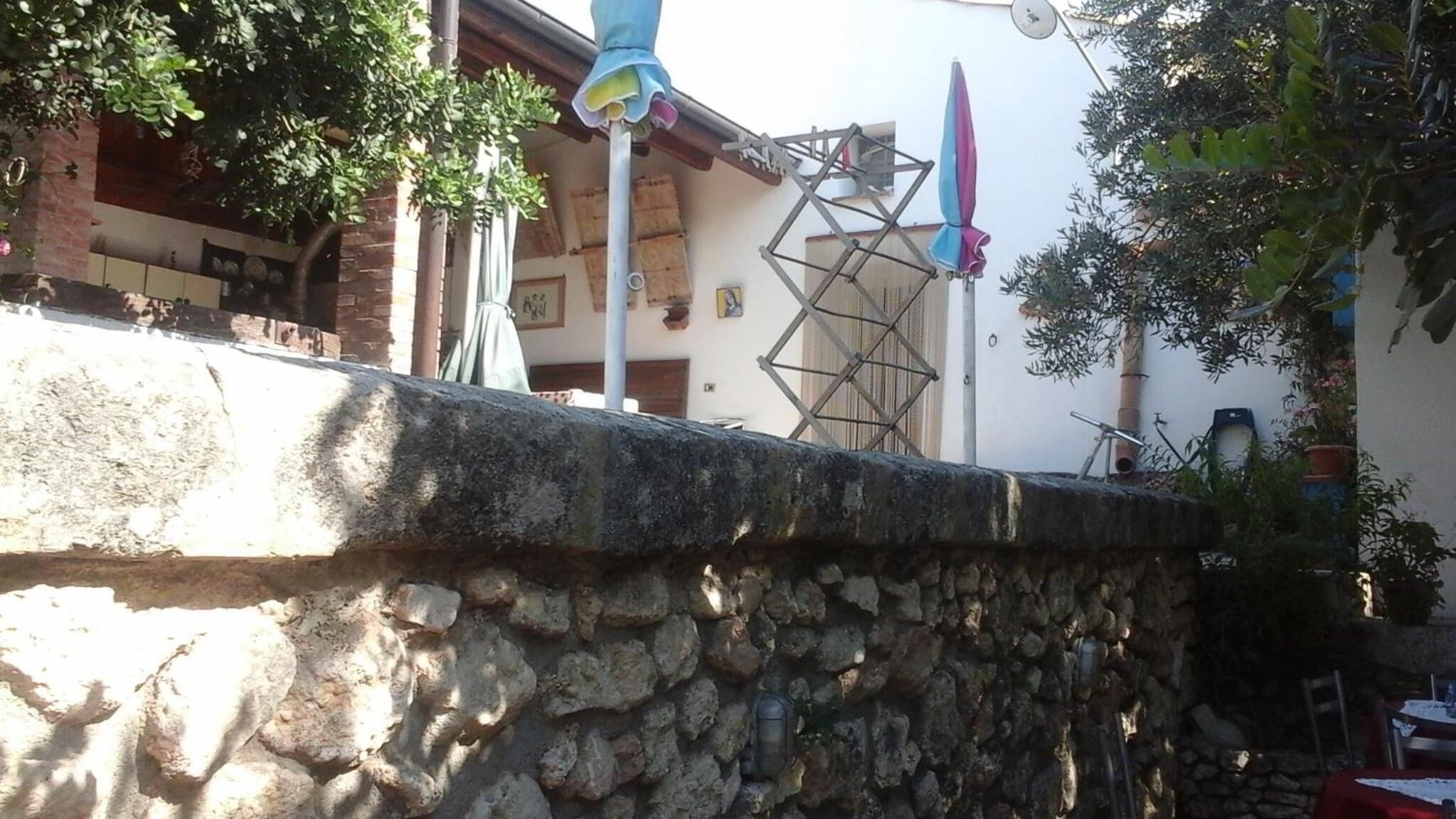 A stone wall with a metal structure on top, a metal pole, and a building with a window and a door in the background.