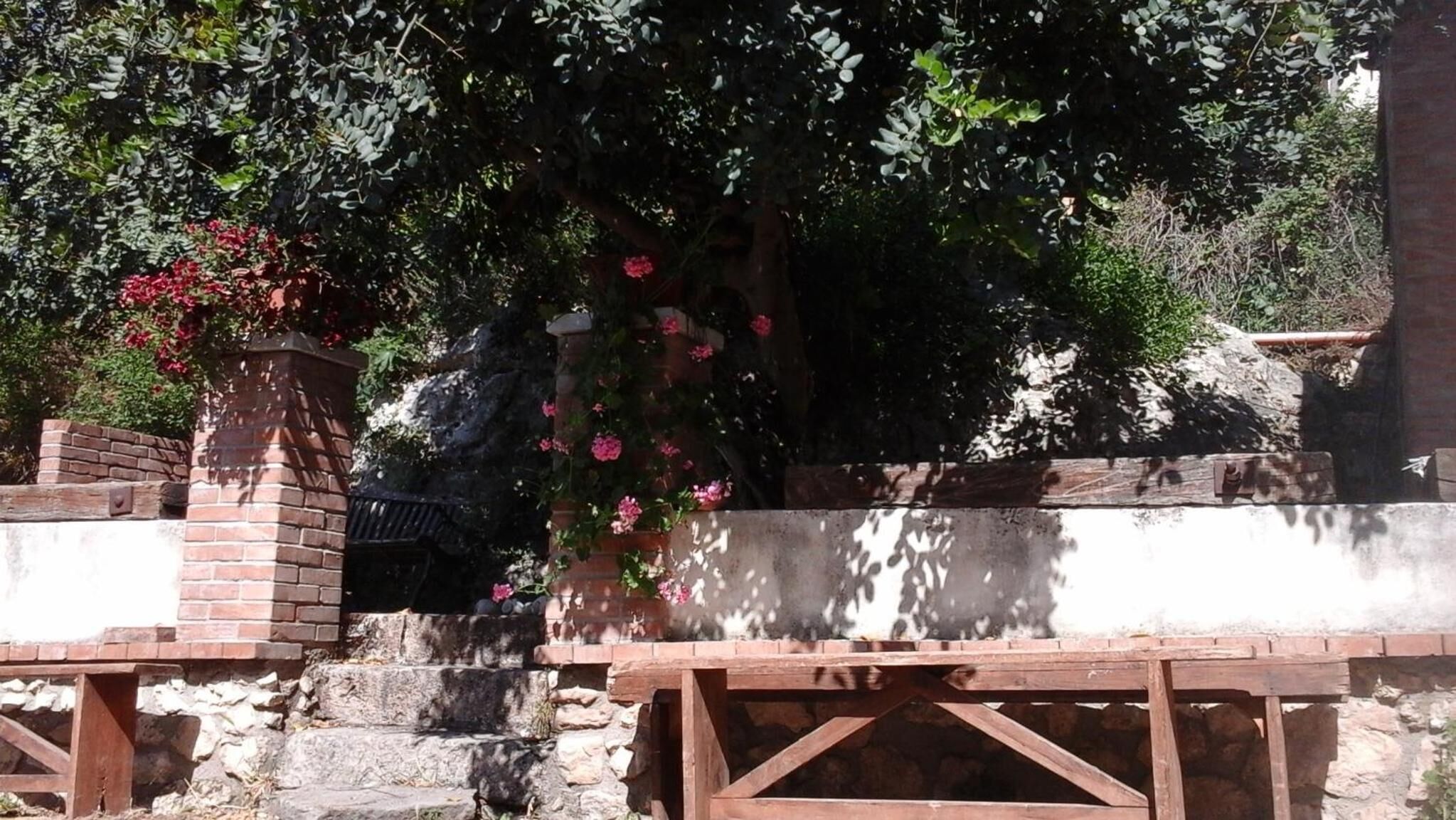Un mur de pedra amb una cadira de fusta i una estructura de maó amb una test de flors.