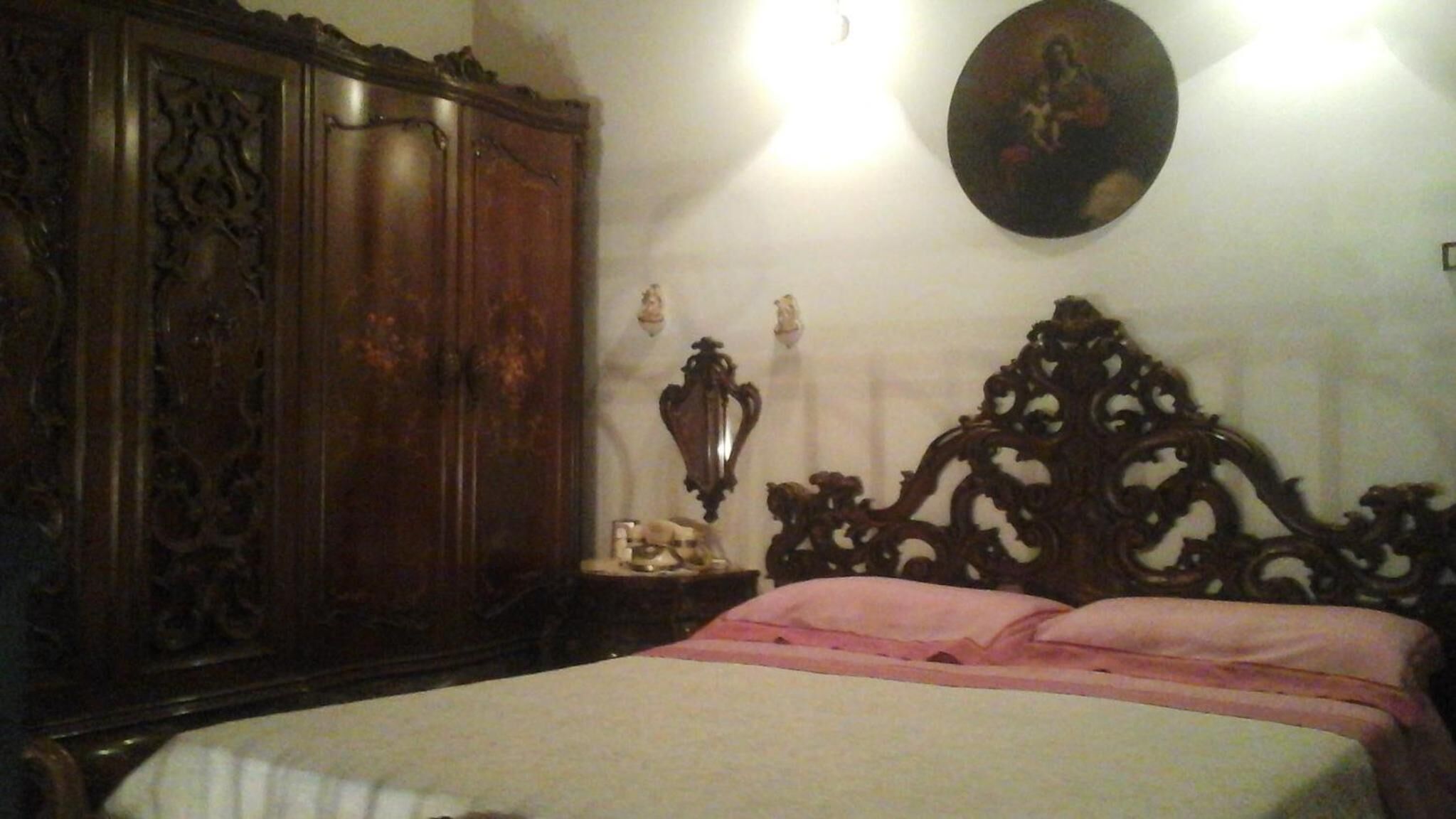 A bedroom with a large wooden wardrobe, a decorative wall hanging, and a bed with pink bedding.