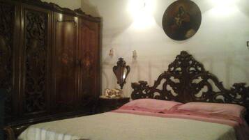 A bedroom with a large wooden wardrobe, a decorative wall hanging, and a bed with pink bedding.